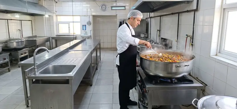 Aşçı buharı tüten kazanda sulu yemeği karıştırıyor